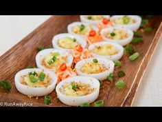 small deviled eggs are arranged on a wooden platter with green onions and garnishes