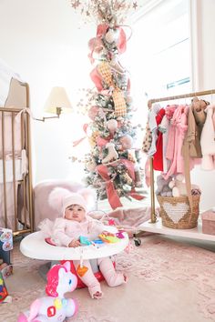 a baby sitting in a highchair next to a christmas tree and stuffed animals