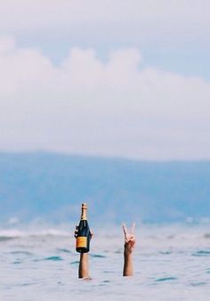 two people in the ocean holding up bottles and pointing at them with their fingers to the sky