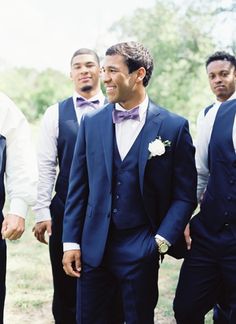 a group of men standing next to each other wearing suits and bow ties with trees in the background