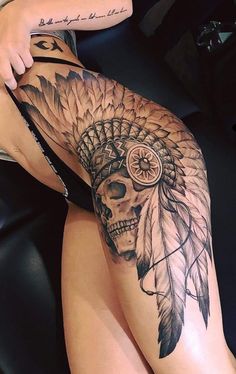 a woman's thigh with a skull and feather headdress tattoo on it