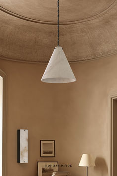 a lamp hanging from the ceiling above a bed in a room with beige walls and furniture