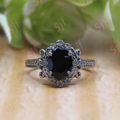 a black diamond ring sitting on top of a wooden table next to green leaves and flowers