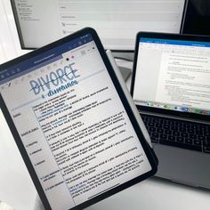 two laptops sitting next to each other on top of a white table with an open book