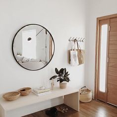 there is a mirror on the wall above a table with two baskets and a potted plant