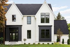 a white house with black shutters on the front and side windows, grass in front