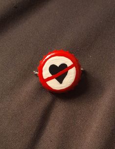 a red and white pin with a black heart in the center on a brown background