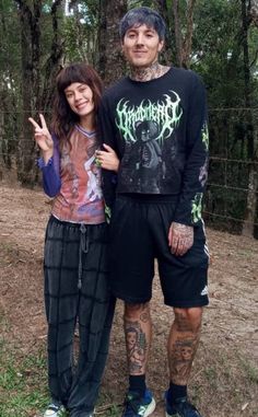 a man and woman standing next to each other in front of some trees with tattoos on their arms