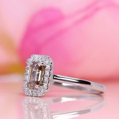 an engagement ring with a large diamond surrounded by smaller diamonds in front of a pink flower