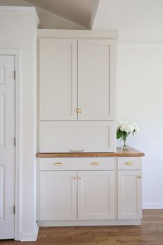 a white kitchen with wooden counter tops and cabinets in front of a door that leads to another room