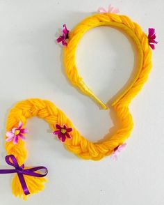 a yellow headband with pink flowers and a purple ribbon around it on a white surface