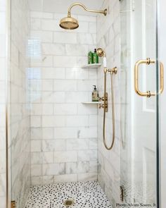 a walk in shower sitting next to a white tiled wall and floor with gold fixtures