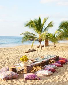 a picnic table set up on the beach with pillows and flowers in front of it