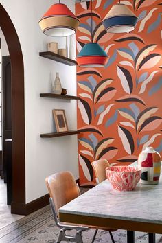 a dining room table and chairs with an orange wallpaper behind it, along with hanging lights