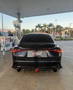 the back end of a black sports car at a gas station with palm trees in the background