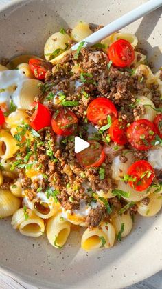 a white bowl filled with pasta and meat topped with tomatoes, cheese and parsley