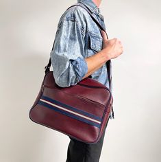 Sporty, yet smart men's shoulder bag in wine red leather imitation vinyl with blue and white stripe detail. It is simple, yet stylish and of a perfect, large size. It has a zip fastening and a front zip pocket, adjustable shoulder strap and metal feet at the bottom. Perfect for weekend breaks or as a carry all for work.  No labels or brand. Leather imitation material. It measures 36 x 26 x 14cm. The strap is 3cm wide and the drop is 42cm long at most. Can be shortened to a top handle length. Exc Retro Burgundy Shoulder Bag For Everyday, Retro Burgundy Bag For Everyday Use, Retro Burgundy Travel Bag, Red School Bag With Luggage Sleeve, Smart Men, Sports Bags Gym, Weekend Breaks, Sport Bag, Wine Red