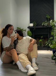 two women sitting on the floor taking pictures with their cell phones while they both wear white socks