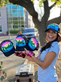 a woman holding three hats with the word candice on them in front of a tree