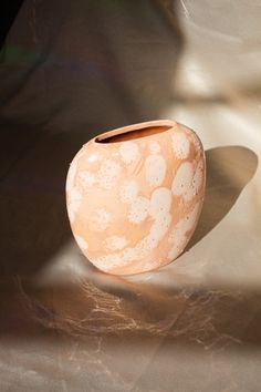 an orange vase sitting on top of a table next to a shadow from the sun