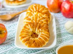 an apple pie on a white plate next to some apples and other food items with spoons