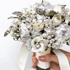 a bridal bouquet with white flowers and pearls is held by a woman's hand