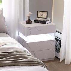 a white bed sitting next to a nightstand with a clock on it's side