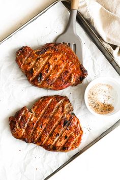 two steaks sitting on top of a pan next to a bowl of seasoning