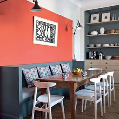 a dining room table with white chairs next to an orange wall