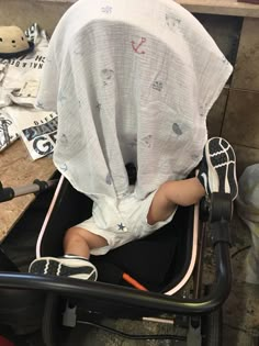 a baby sitting in a stroller with a sheet over it's head and legs