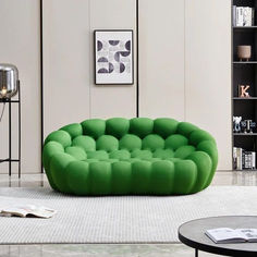 a green couch sitting on top of a white floor next to a book shelf filled with books