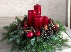 three red candles sitting on top of a christmas wreath with pine cones and ornaments around it