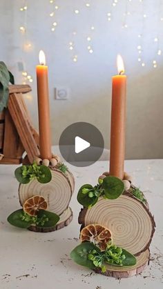 two candles are sitting next to each other on a table with green leaves and orange slices