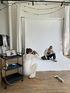 two people are sitting on the floor in front of a white backdrop and lighting equipment