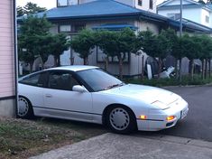 a white car is parked on the side of the road in front of a house