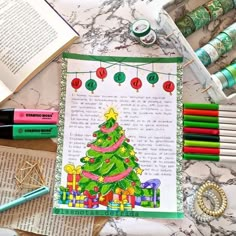 an open book with christmas tree on it next to crayons, markers and pencils