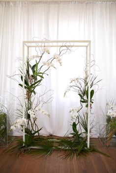 an arrangement of flowers and greenery in front of a white curtain