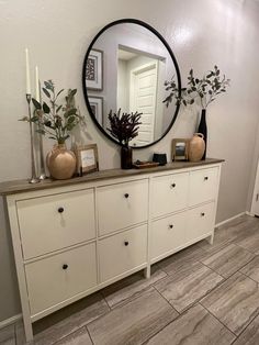 a white dresser topped with lots of drawers under a round mirror