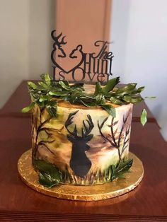 a cake decorated with deer and leaves on a wooden table next to a metal sign