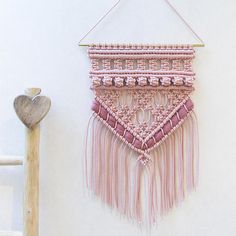 a pink wall hanging next to a wooden stick and heart shaped object on the wall