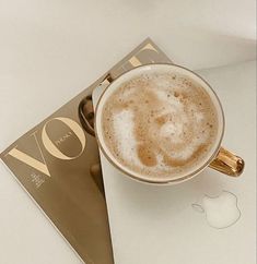 a cup of coffee sitting on top of a white table next to an apple book