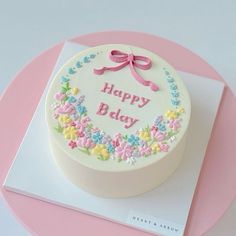 a birthday cake decorated with flowers and a pink ribbon on a white tablecloth that says happy bday