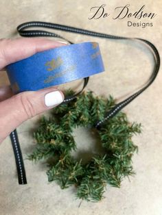 a hand holding a blue wristband with a wreath on the side and black cord attached to it