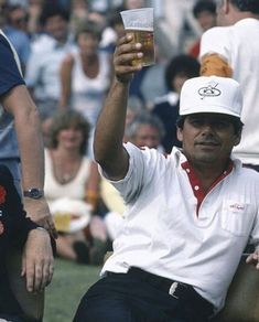 a man sitting in a chair holding up a glass of beer at a sporting event