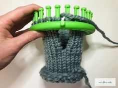 a hand holding a green and gray knitted brush holder with yarn on it's sides