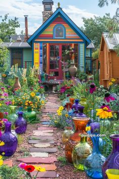 colorful vases are lined up in front of a small house with flowers on the ground