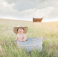 a baby wearing a cowboy hat sitting in a bucket on top of a grass covered field