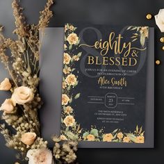 an elegant wedding card with gold lettering and flowers on the front is surrounded by greenery