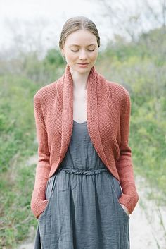 a woman standing on a path wearing a gray dress and red cardigan sweater over her shoulders