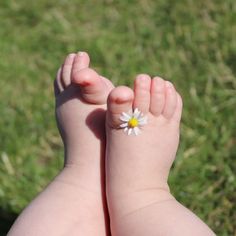 a baby's foot with a small flower on it and grass in the background